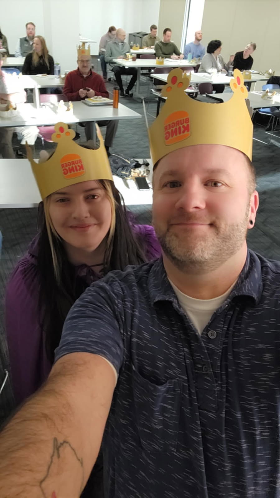 Selfie of a man and woman wearing a crown, in a meeting.